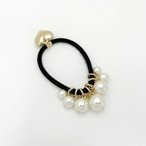 Détail d'un élastique à cheveux perle et cœur avec pendentif doré sur fond neutre