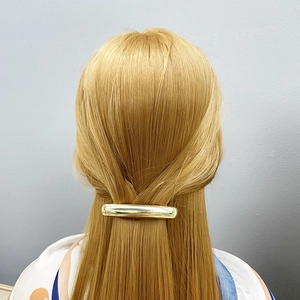 Minimalist golden polished tubular metal hair clip shown on blonde hair from a back view