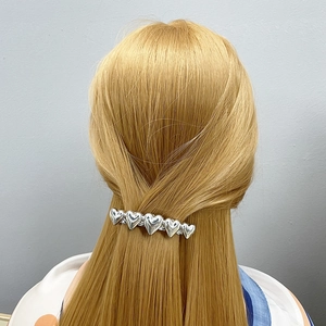 Detail of silver heart shaped hair clip worn on straight blonde hair from the back view