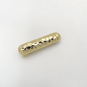 Detail of a golden hammered metal spring hair clip featuring a textured wavy finish