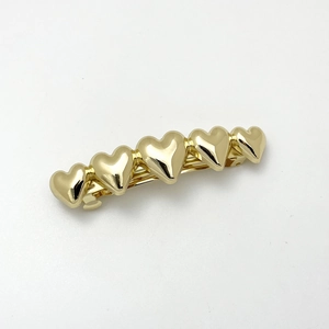 Detail of five linked gold heart elements on a polished metal hair clip with spring closure