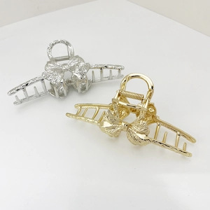 Detailed view of metal bow hair claws with pleated texture in silver and gold finishes