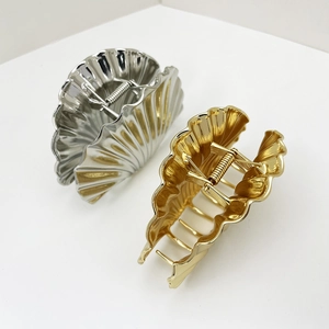 Macro detail of glossy gold and silver shell-shaped metal hair claws with pleated texture
