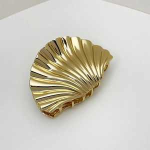 Macro shot of polished gold shell hair claw clip showing 3D texture and metallic finish