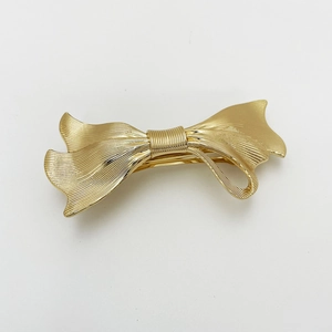 Detailed view of golden metal bow hair clip with elegant wave texture and spring closure