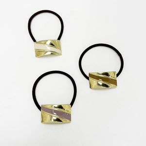 Close-up of three gold-plated metal hair ties with cream, brown, and pink resin inserts
