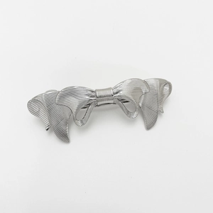 Macro shot of a silver metal hair clip with a layered ribbon bow and brushed texture detail