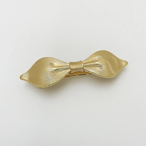 Detailed macro view of the gold-tone metal bow hair clip with textured vertical stripes