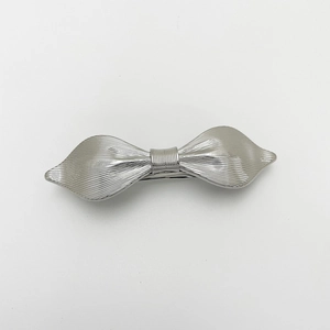 Detail of silver alloy bow hair clip with vertical brushed metal texture and spring clip
