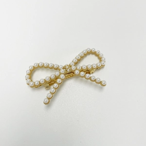 Detailed macro view of a golden bow hair clip with polished white imitation pearls