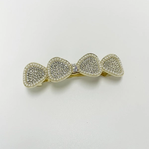 Detailed view of golden metal bow hair clip with white pearls and sparkling rhinestones
