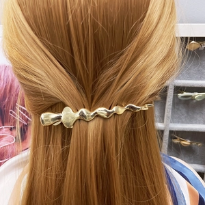 Golden irregular wavy metal hair clip shown worn on light brown straight hair