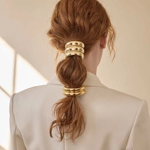 Detailed view of polished gold U-shaped metal hair cuffs on a low ponytail hairstyle