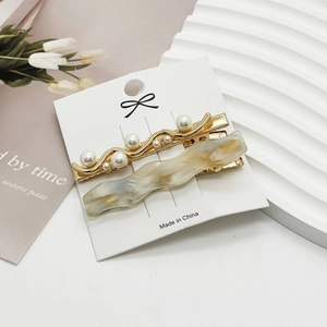 Detailed set of a gold pearl duckbill clip and amber resin hair pin on a display card