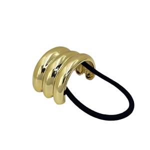 Gold wavy metal ponytail holder with black elastic band on a white background