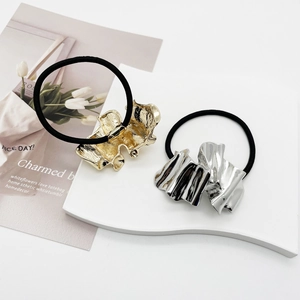 Irregular gold and silver pleated metal hair ties on a minimalist display board