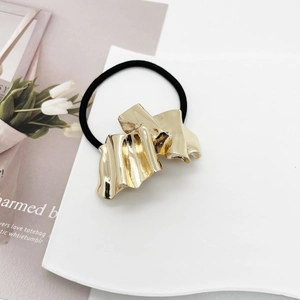 Close-up of golden wavy alloy hair tie with black elastic cord on artistic background