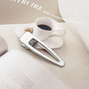Detail of silver brushed metal teardrop hair clip showing the matte texture and spring mechanism