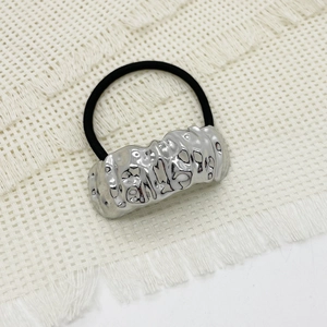 Detail of silver hammered metal buckle on black elastic hair tie on white fabric