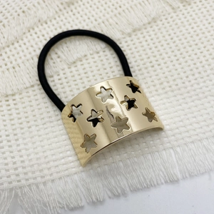 Detail of black elastic hair tie with golden star-patterned metal cuff on woven background