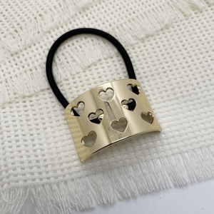 Detail of golden heart-shaped cutout metal hair ring with black elastic band on white fabric