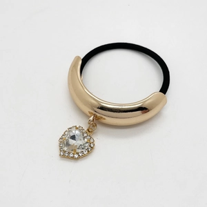 Close-up of heart-shaped crystal pendant and polished gold metal tube on hair tie