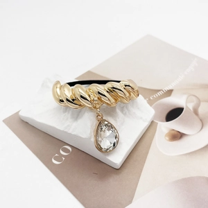 Detail of gold twisted metal hair tie with clear teardrop pendant on white stone