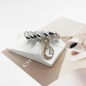 Detail of twisted silver ring featuring a pear-cut crystal charm on stone base