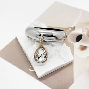 Detail of silver U-shaped ponytail holder with teardrop crystal charm on white stone