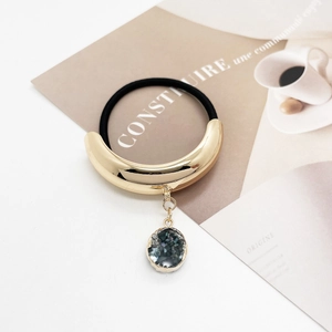 Macro detail of golden U-shaped alloy hair tie with dark shimmering round pendant
