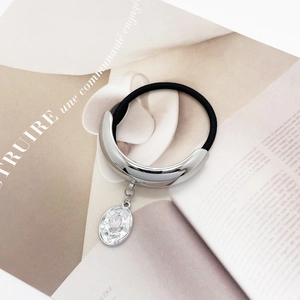 Close-up of U-shaped silver hair tie with pink teardrop pendant on magazine