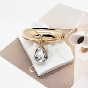 Close-up of golden U-shaped hair cuff with a faceted teardrop crystal pendant