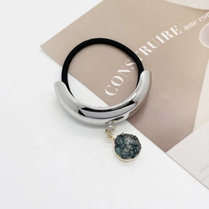 Macro shot of silver C-shaped metal hair tie with dark crystal pendant on magazine background