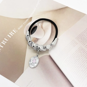 Detailed macro view of a silver metal pendant with a pink stone on a black elastic hair tie