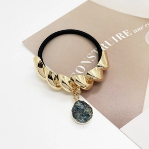 Detail of a black elastic hair tie with a gold twisted metal tube and a grey crystal drop