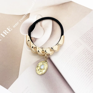 U-shaped gold alloy hair tie with light blue gemstone pendant on a magazine background