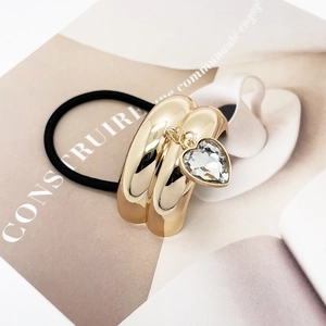 Detail of golden U-shaped hair tie with crystal heart pendant on a white background