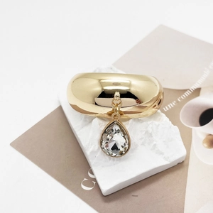 Detail of a U-shaped gold hair tie with a crystal teardrop pendant on marble stone