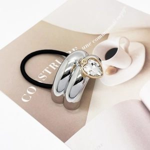 Close-up of silver U-shaped hair tie with a crystal heart charm on a magazine background