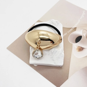 Detail of a U-shaped gold alloy hair tie with a clear crystal water drop charm