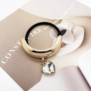 Detail of black elastic hair tie with golden U-shaped metal and heart crystal pendant