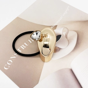 Close-up of black elastic hair tie with heart-shaped crystal on gold metal hardware