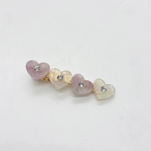 Détail de quatre barrettes en cœur en résine avec strass brillants sur base en métal doré