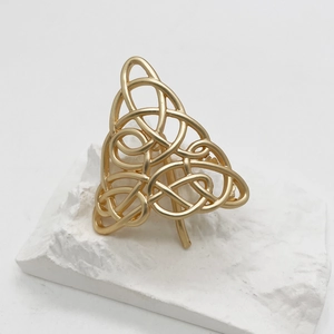 Close-up of golden alloy Celtic knot hair clip with matte texture on a stone base