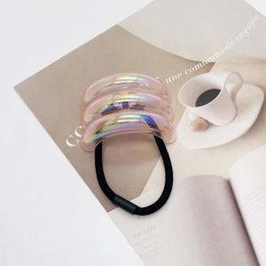 Detail of a U-shaped iridescent pink hair tie set on a magazine with soft lighting