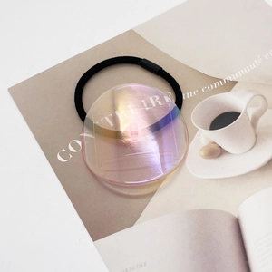 Detail view of aurora translucent round charm on black elastic hair tie with magazine