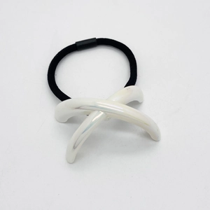 Détail d'un élastique à cheveux noir avec un accessoire croisé blanc effet nacre brillant