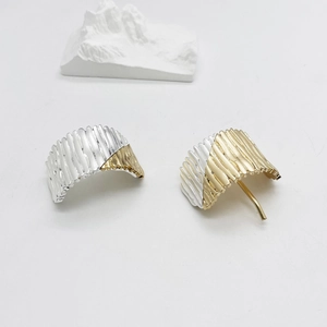 Detailed macro view of two-tone pleated metal hoop earrings with silver and gold texture