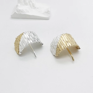 Macro shot of textured two-tone gold and silver metal earrings with radial wing-like patterns