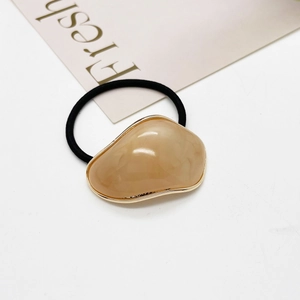 Détail d'un élastique à cheveux beige de forme galet avec bordure dorée raffinée
